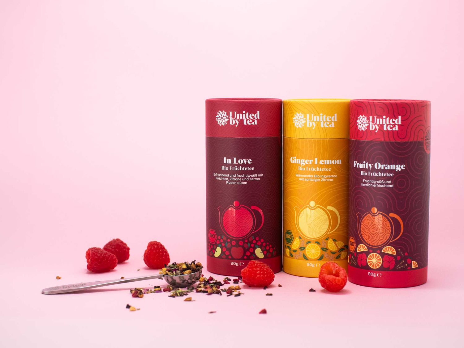 Drei Dosen der losen Bio-Früchtetees "Fruity Orange", "Ginger Lemon" und Fruity Orange" mit Teemesslöffel und Himbeeren